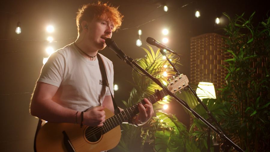 Matt Keddie singing with an acoustic guitar under warm festoon lights