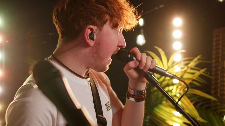 Close-up of Matt Keddie singing into a handheld mic, wearing in-ear monitors