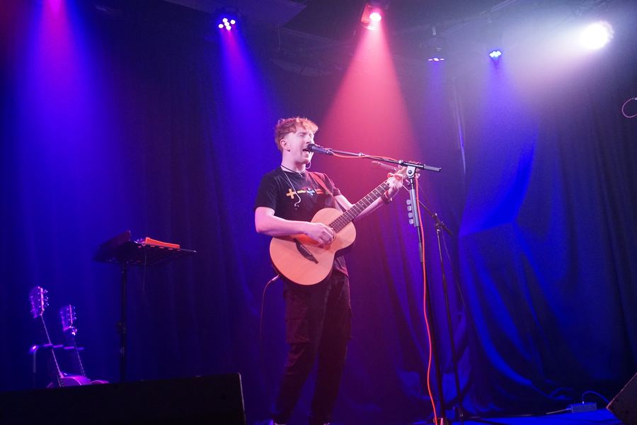 Matt Keddie singing with an acoustic guitar under purple and pink stage lights