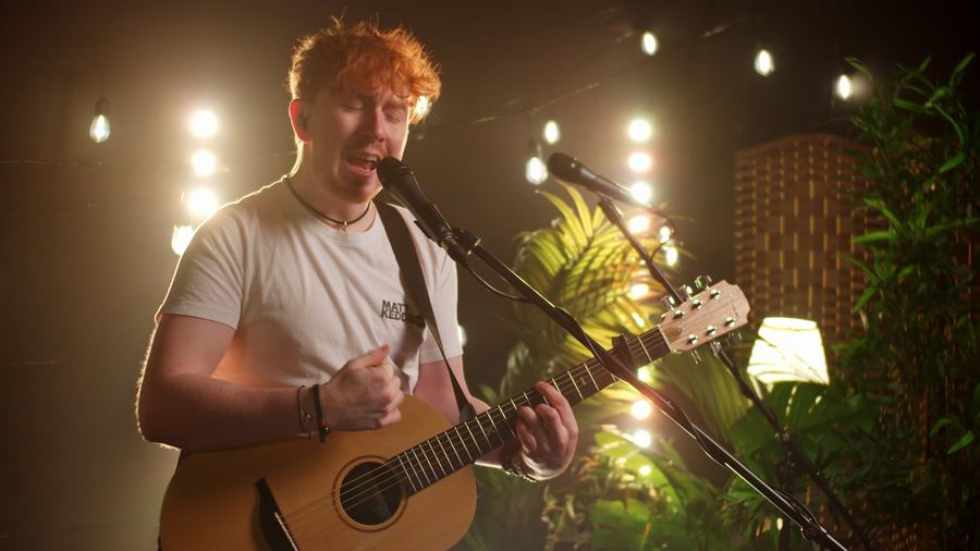 Matt Keddie singing with eyes closed, strumming an acoustic guitar