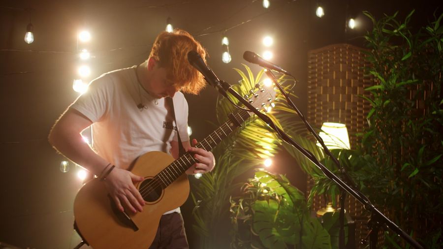Matt Keddie looking down at his guitar mid-song, lit from behind