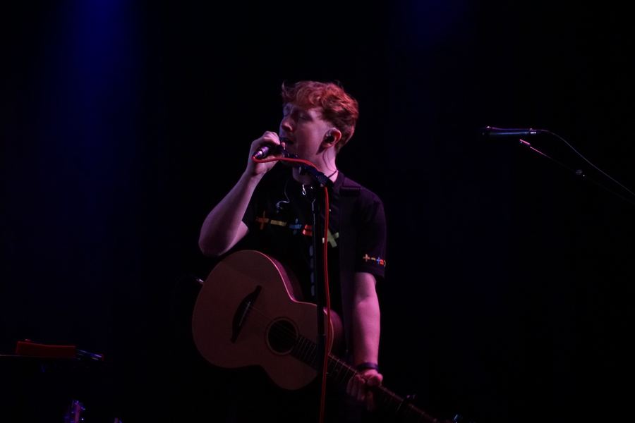 Matt Keddie singing into a handheld mic, guitar slung low